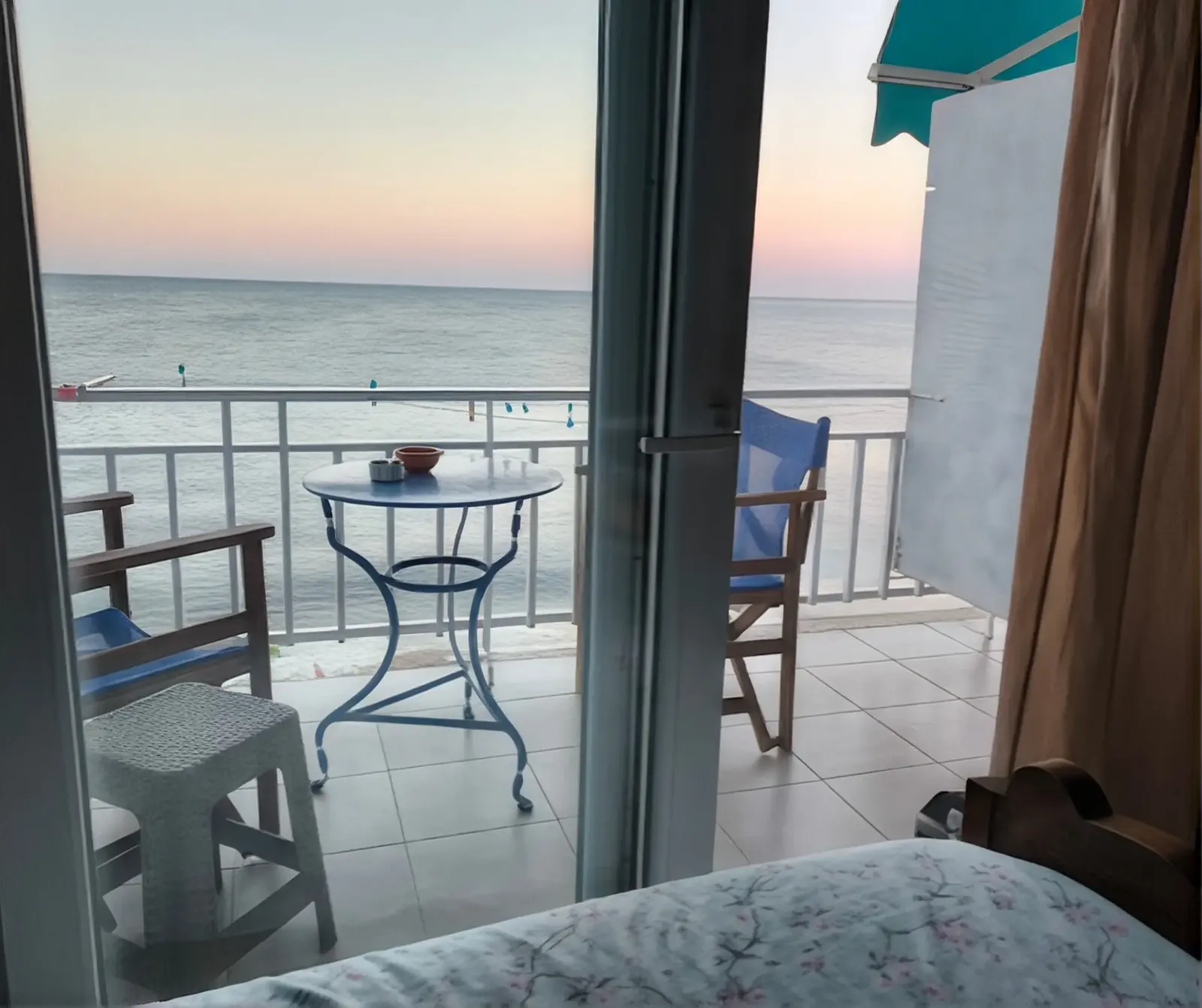 Balcony of a sea-view apartment at dusk, with a small table, chairs and the sea beyond the railing